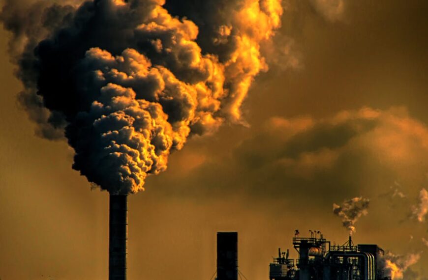 A factory emitting smoke clouds against a dark sunset sky, illustrating air pollution and industrial impact.