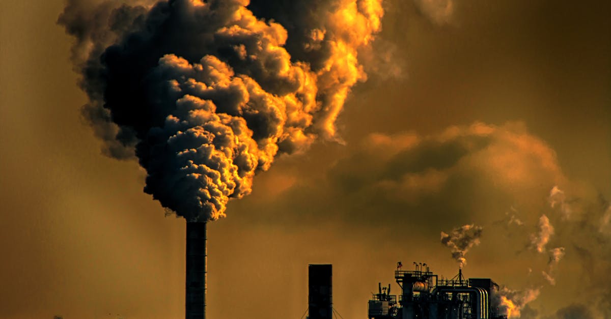 A factory emitting smoke clouds against a dark sunset sky, illustrating air pollution and industrial impact.